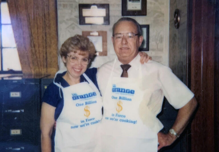 Joyce Pipes and Paul Pipes standing in Pipes Insurance Service office with Grange Insurance aprons on